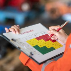 Action of a person is using ballpoint pen to marking on the risk assessment matrix table at "High risk" level. Industrial or business working action scene photo. Close-up and selective focus.